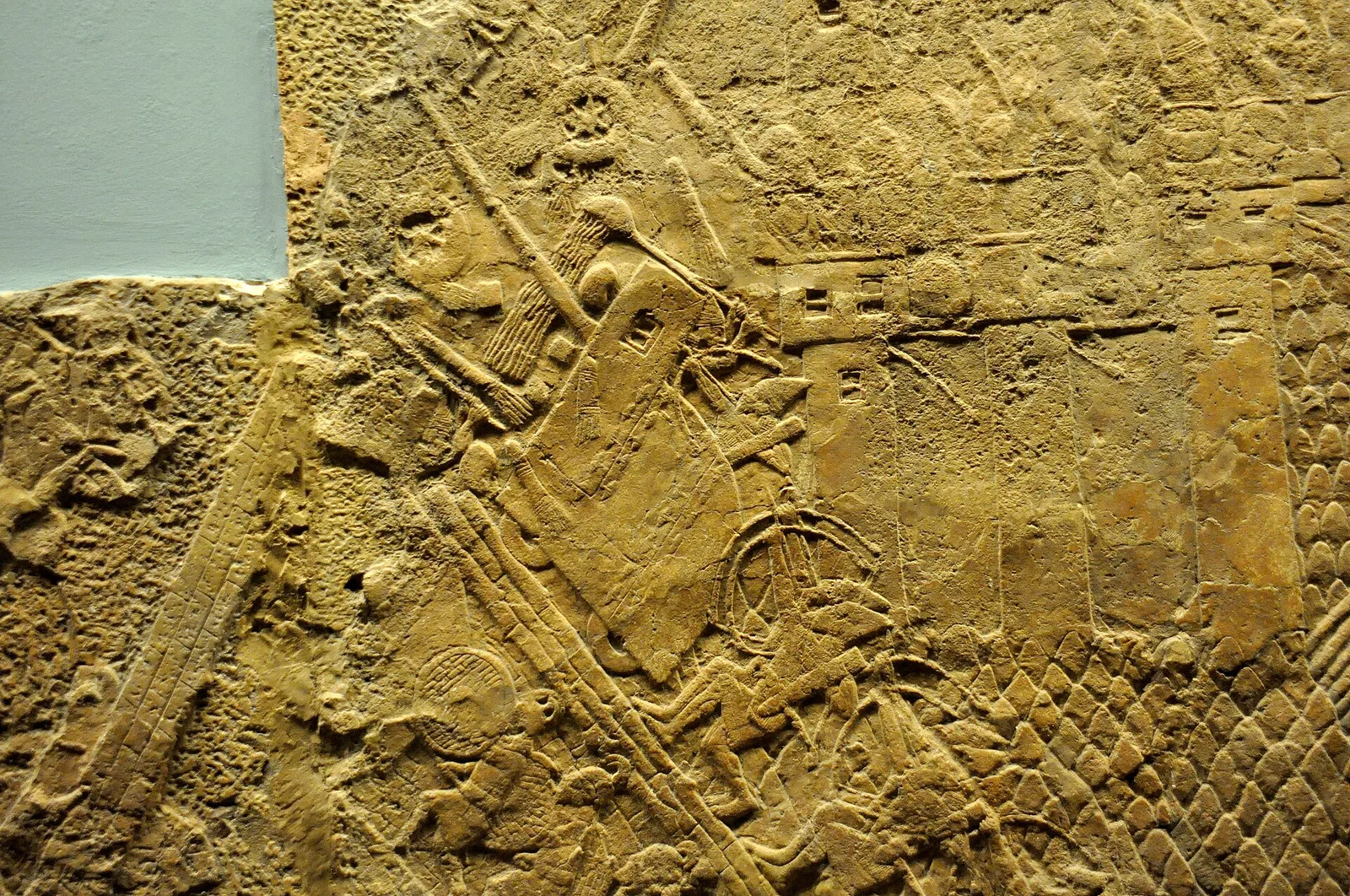 Carved Assyrian relief of a siege engine climbing a ramp toward a city wall